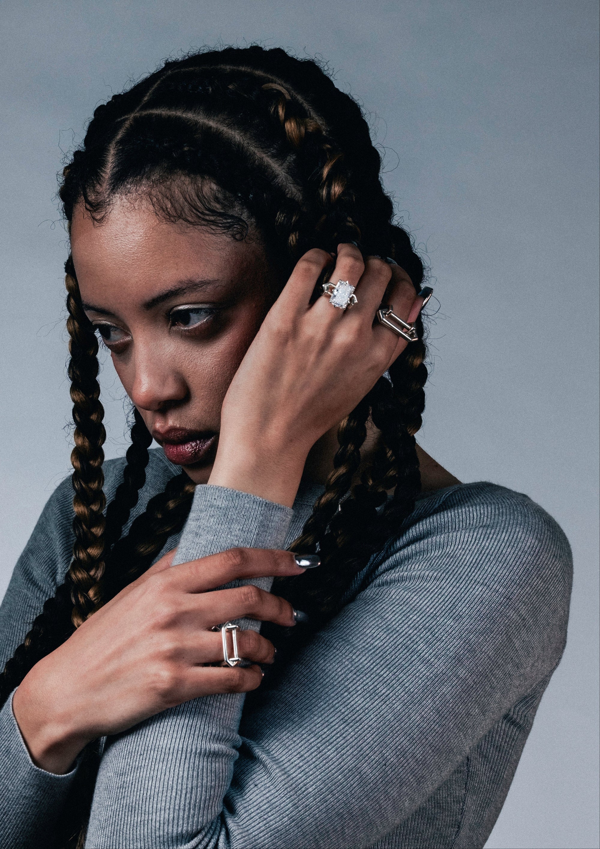 Woman with braided hair wearing multiple edgy, brutal, contemporary silver rings on a gray background